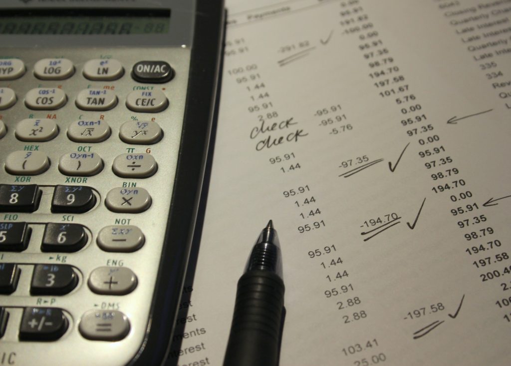 Close up image of a calculator and pen on top of a printout of a monthly budget