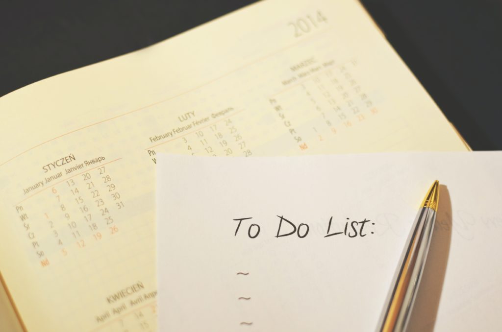 Image of a piece of paper laying on top of a calendar.  The paper has the words to do list written across the top and a pen is resting on the page.