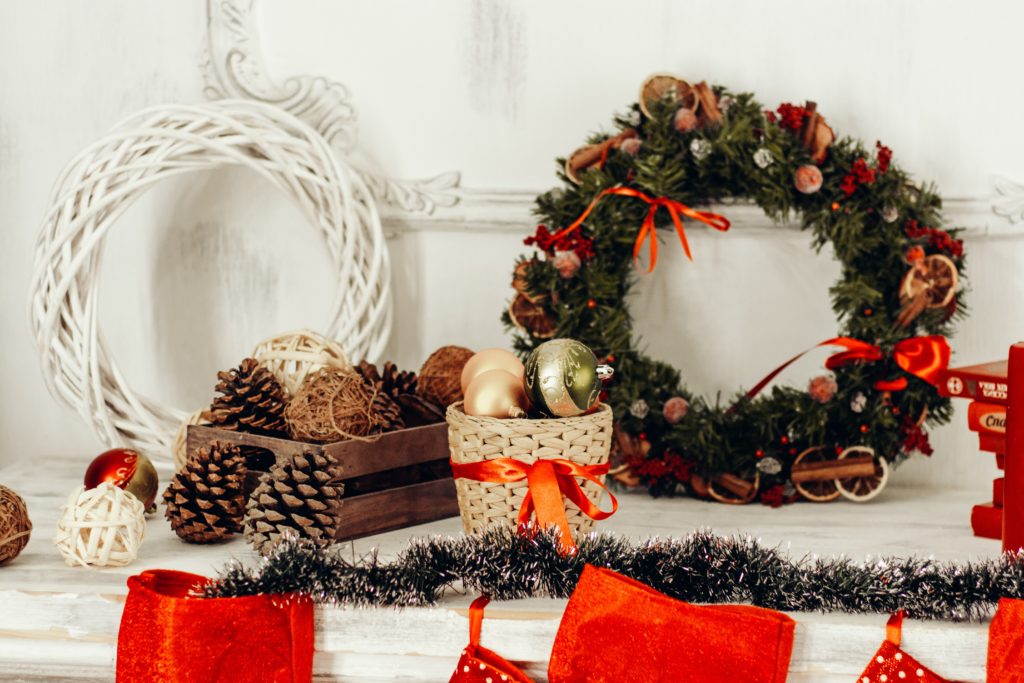 Image of a mantle decorated with winter holiday items including a wreath, pinecones, and gold tree ornaments in a small basket with a red ribbon