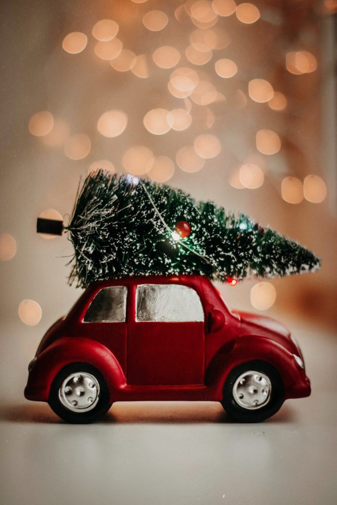 Image of a miniature red, two door  car with a Christmas tree on the roof.