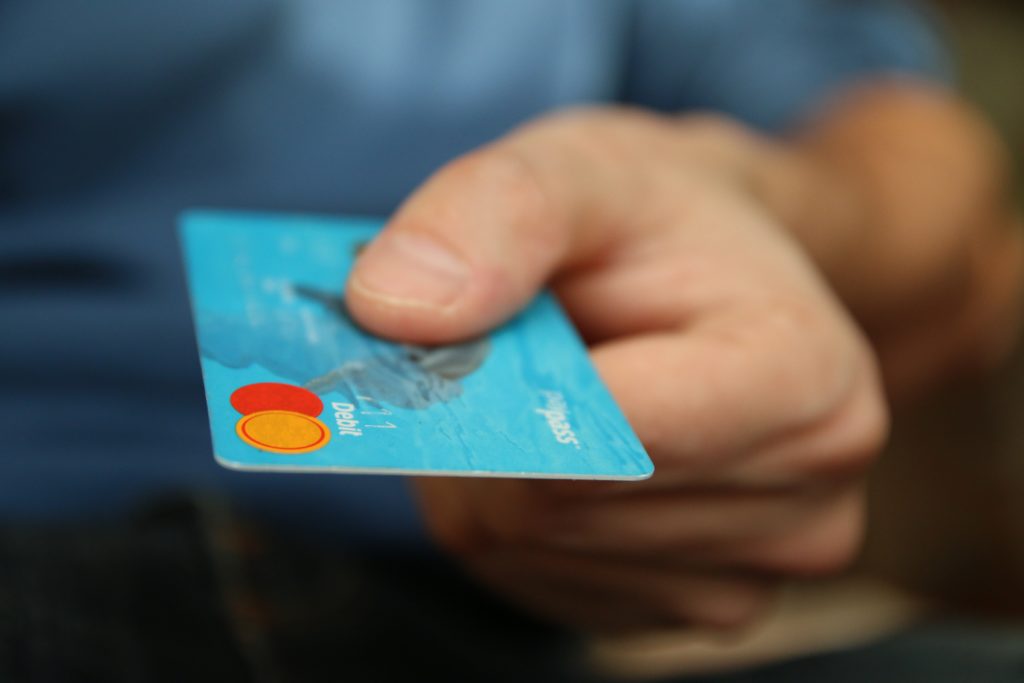 Close up of a man's hand as viewed from the font.  He is holding  a credit card and appears to be in the process of handing it to an unseen person.