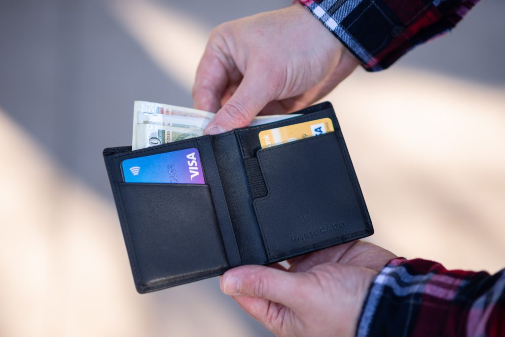 Man holding an open black bifold wallet containing credit cards.  He is removing several dollar bills.
