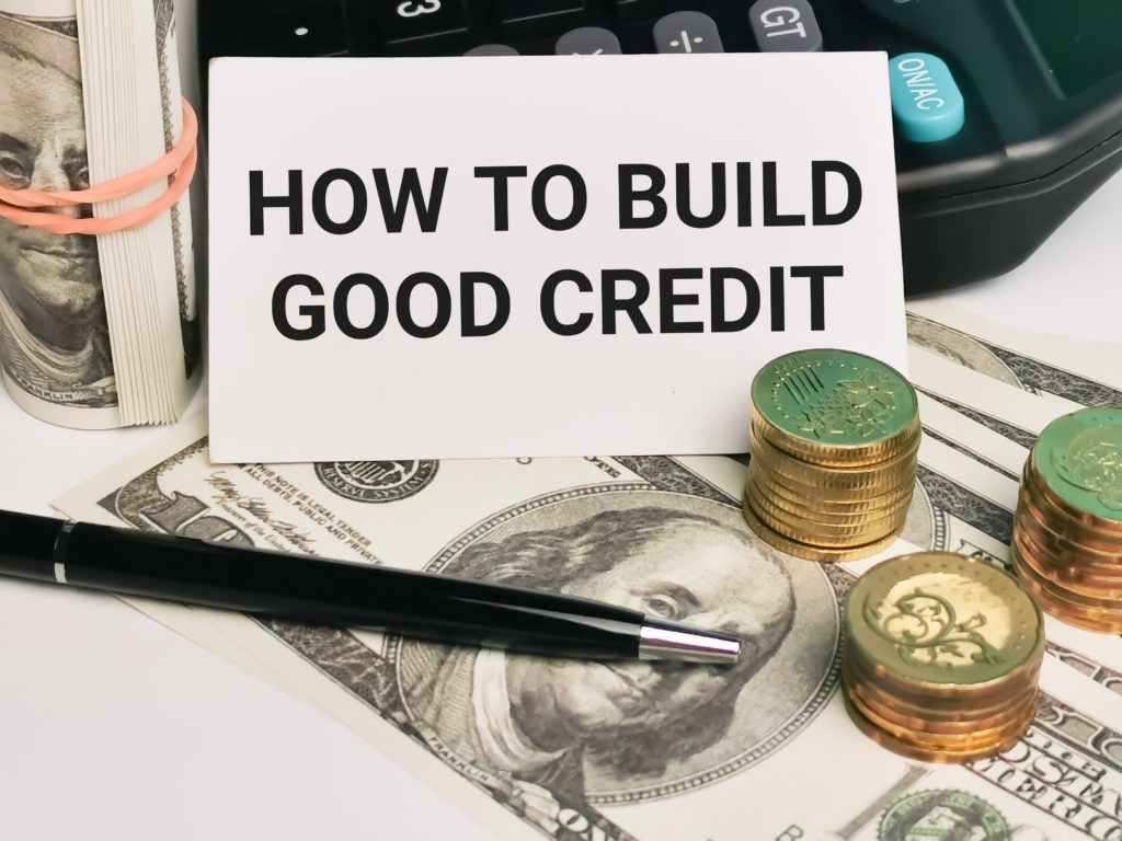 white card written HOW TO BUILD GOOD CREDIT with calculator, a pen, coins and fake money