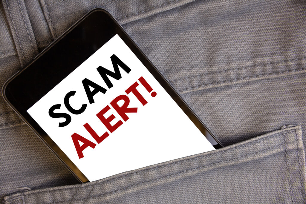  cell phone into jean pocket white screen black and red letters reading scam alert