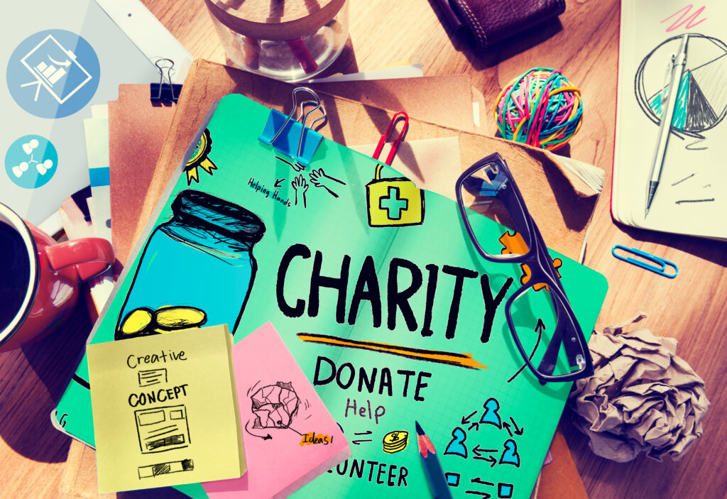 Stylized image of a paper sign on a  cluttered desk.  The sign says charity, donate, and help