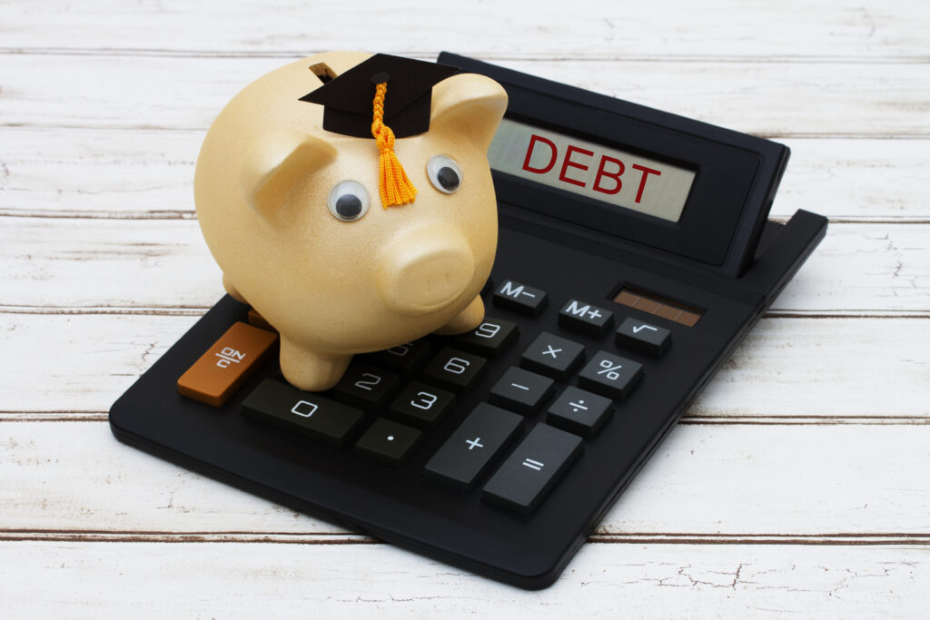A golden piggy bank with a grad hat on a calculator with word Debt over a distressed wood background