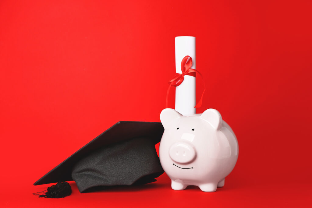 Graduation hat, piggy bank and diploma on red background