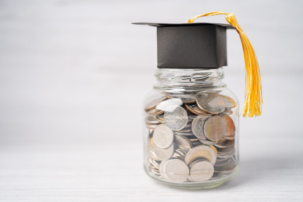 Clear glass jar filled with coins topped with a black graduation cap with a yellow tassel