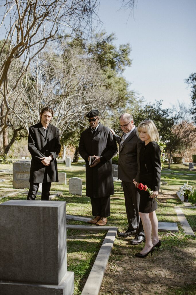 a woman and three men all dressed in black standing in front of a gravesite
